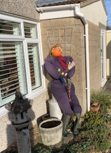 A scarecrow in a boiler suit with a pumpkin for a head, leaning against the wall